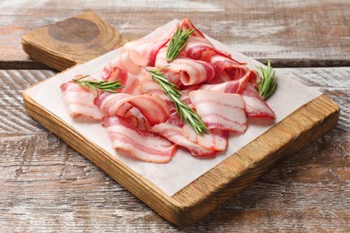 Photo of Slices of raw bacon and rosemary on wooden table