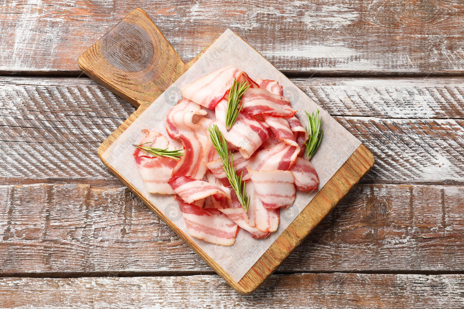 Photo of Slices of raw bacon and rosemary on wooden table, top view