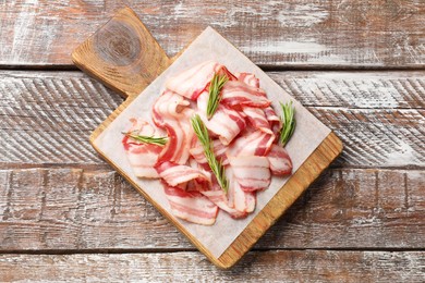 Slices of raw bacon and rosemary on wooden table, top view