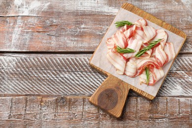 Slices of raw bacon and rosemary on wooden table, top view. Space for text