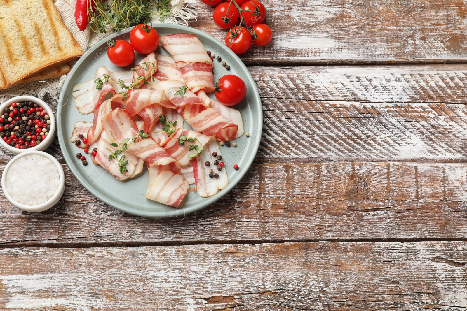 Photo of Slices of raw bacon, spices, bread and tomatoes on wooden table, flat lay. Space for text