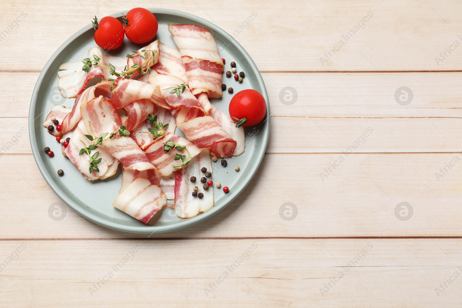 Photo of Slices of raw bacon, spices and tomatoes on wooden table, top view. Space for text