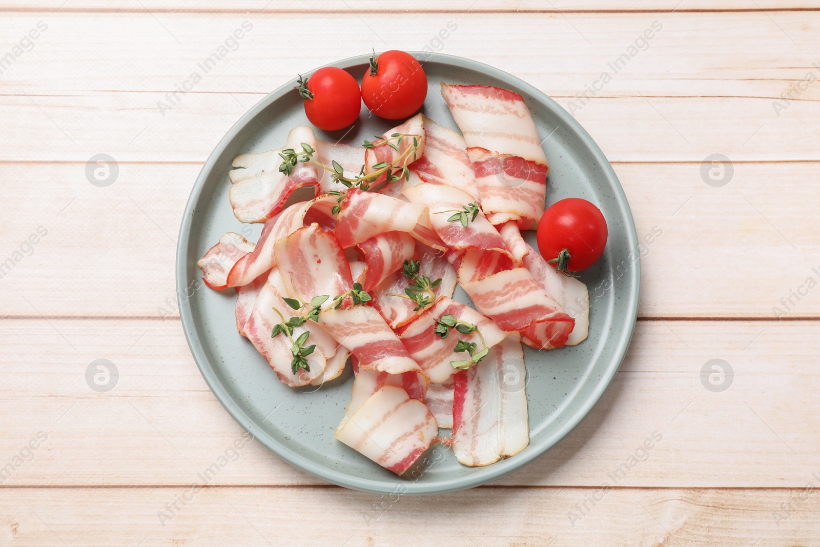 Photo of Slices of raw bacon, microgreens and tomatoes on wooden table, top view