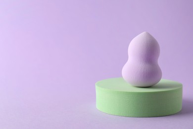 Stylish presentation of makeup sponge on violet background, space for text