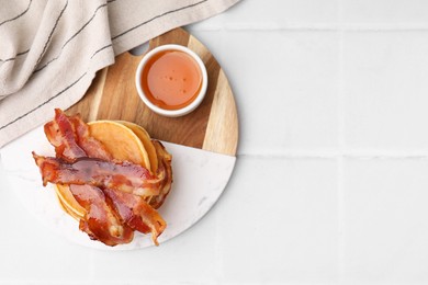 Photo of Delicious pancakes with bacon and honey on white tiled table, top view. Space for text