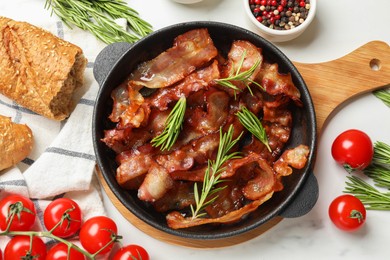 Photo of Delicious bacon slices in frying pan, spices and tomatoes on white table, flat lay