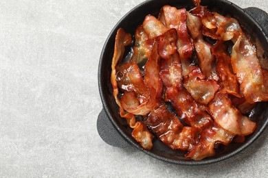 Delicious bacon slices in frying pan on light grey table, top view. Space for text