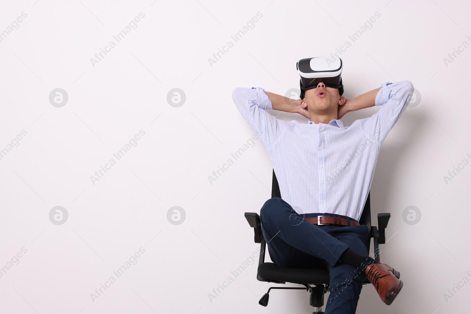 Photo of Emotional young man with virtual reality headset sitting on chair near white wall, space for text