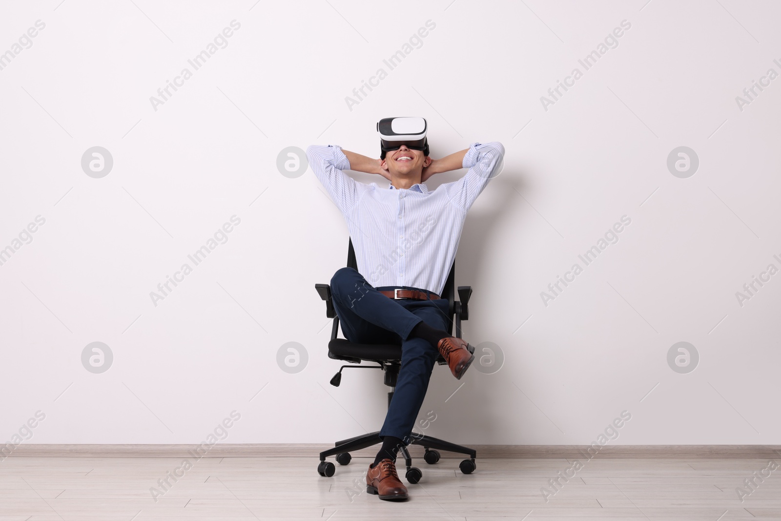 Photo of Happy young man with virtual reality headset sitting on chair near white wall