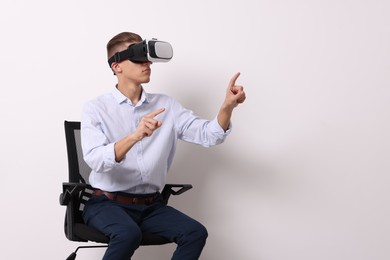 Photo of Happy young man with virtual reality headset sitting on chair near white wall, space for text