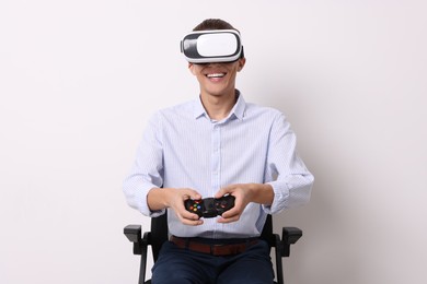 Photo of Happy young man with virtual reality headset and controller sitting on chair near white wall