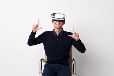 Photo of Happy young man with virtual reality headset sitting on chair near white wall