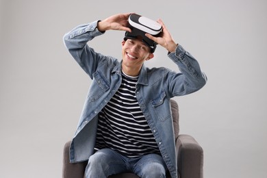 Photo of Happy young man with virtual reality headset sitting on armchair against light grey background