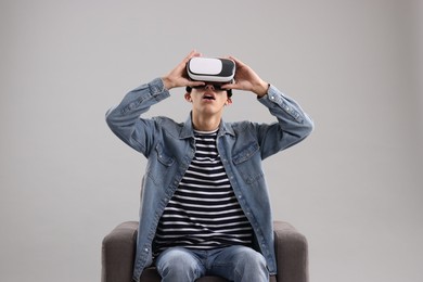 Photo of Emotional young man with virtual reality headset sitting on armchair against light grey background