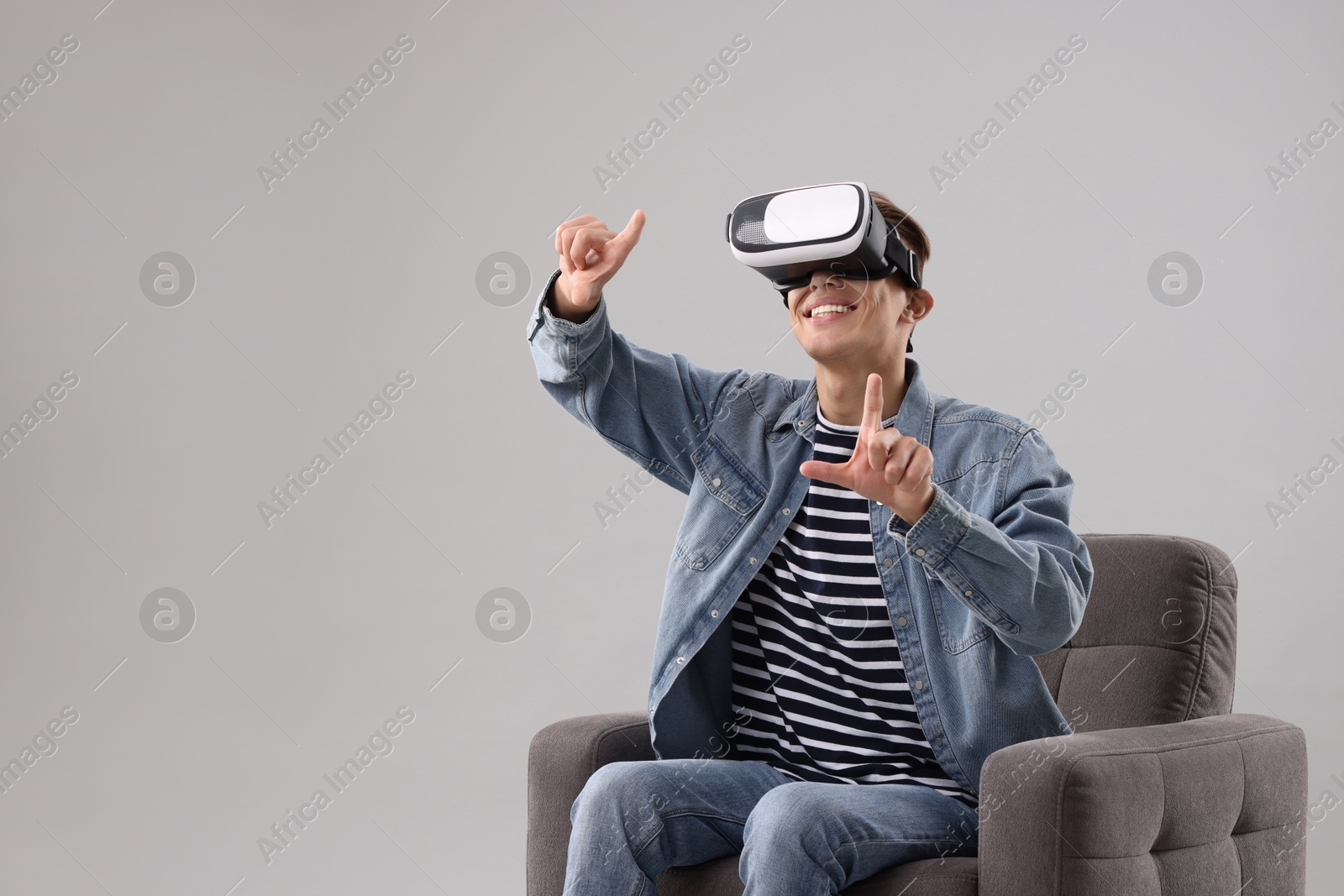 Photo of Happy young man with virtual reality headset sitting on armchair against light grey background, space for text