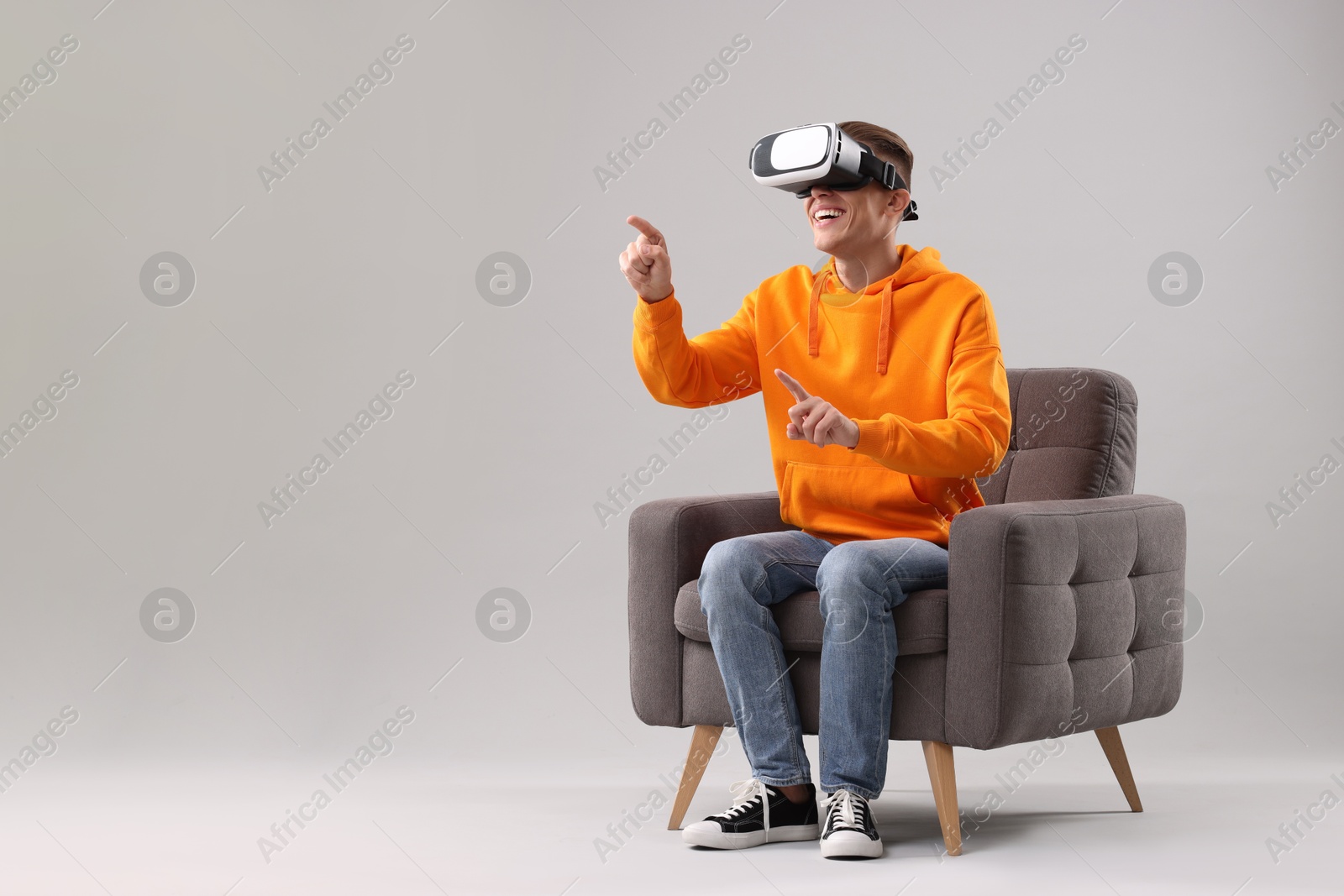 Photo of Happy young man with virtual reality headset sitting on armchair against light grey background, space for text