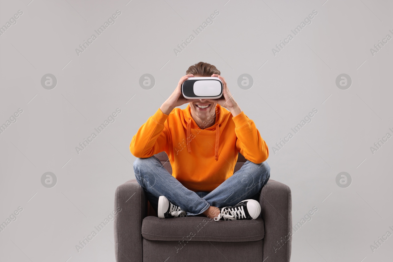 Photo of Happy young man with virtual reality headset sitting on armchair against light grey background