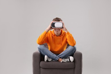 Photo of Happy young man with virtual reality headset sitting on armchair against light grey background