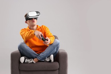 Photo of Emotional young man with virtual reality headset and controller sitting on armchair against light grey background