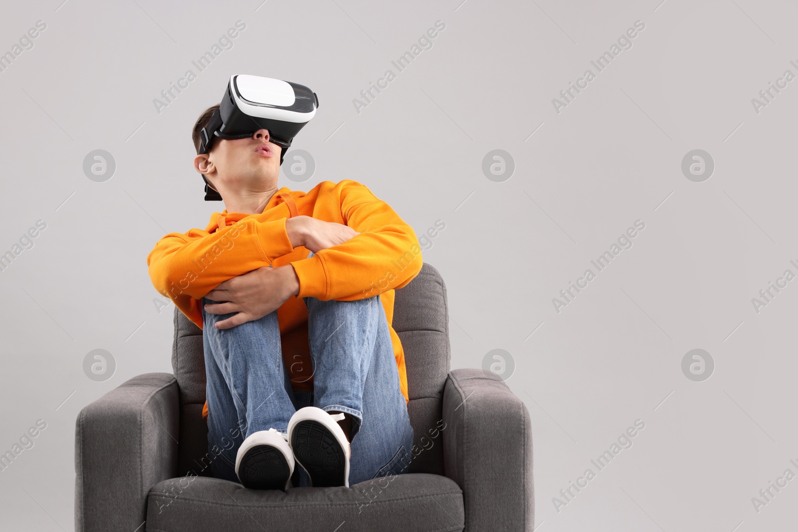 Photo of Emotional young man with virtual reality headset sitting on armchair against light grey background, space for text