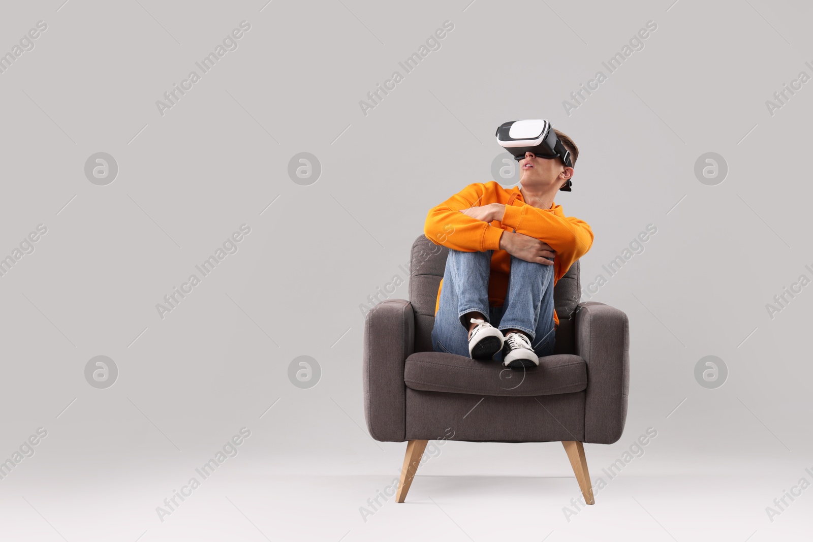 Photo of Emotional young man with virtual reality headset sitting on armchair against light grey background, space for text