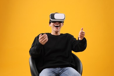 Happy young man with virtual reality headset sitting on chair against yellow background