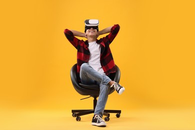 Photo of Happy young man with virtual reality headset sitting on chair against yellow background