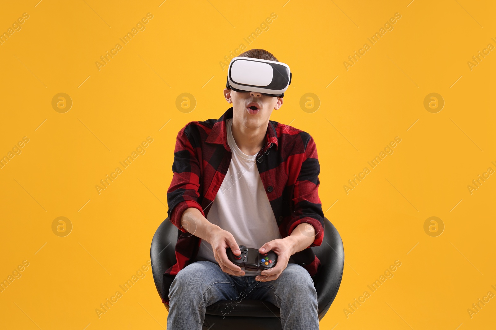 Photo of Emotional young man with virtual reality headset and controller sitting on chair against yellow background