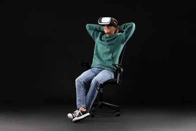 Photo of Happy young man with virtual reality headset sitting on chair against black background