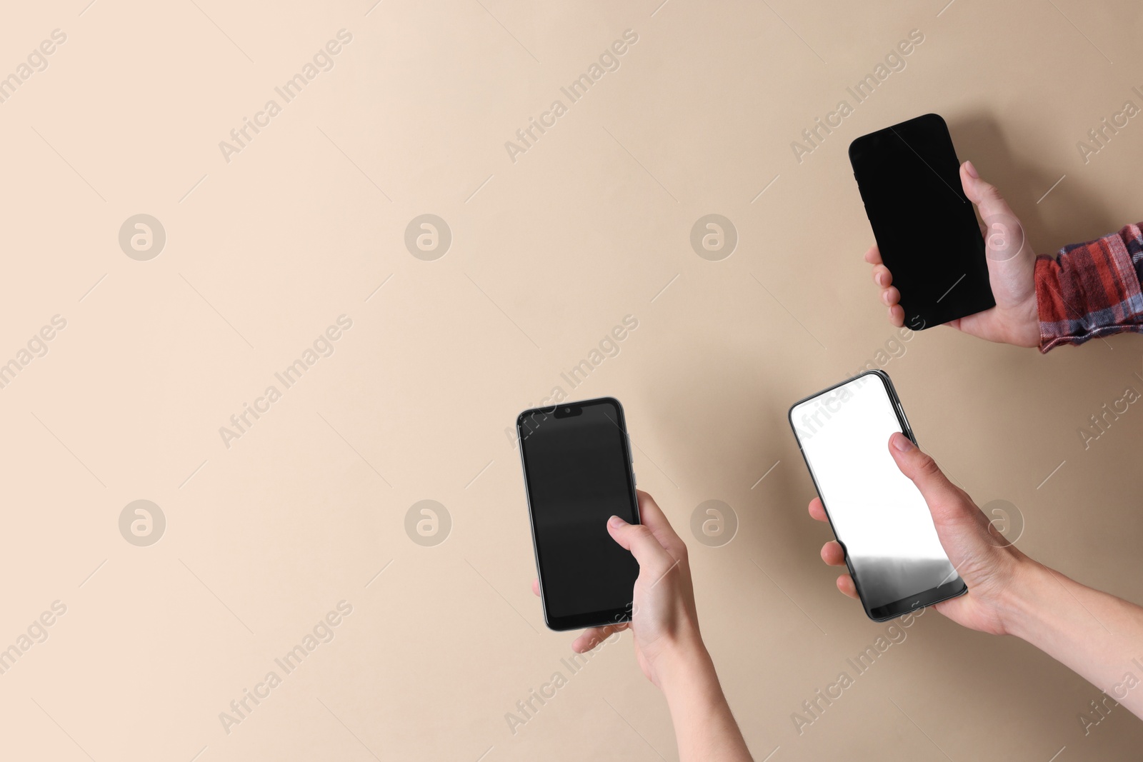 Photo of Women holding smartphones with blank screens against beige background, closeup. Mockup for design