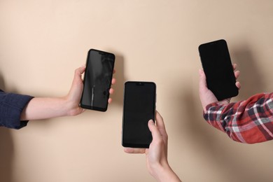 Photo of Women holding smartphones with blank screens against beige background, closeup. Mockup for design