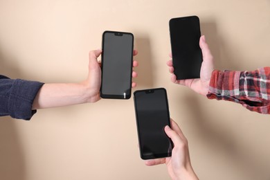 Photo of Women holding smartphones with blank screens against beige background, closeup. Mockup for design