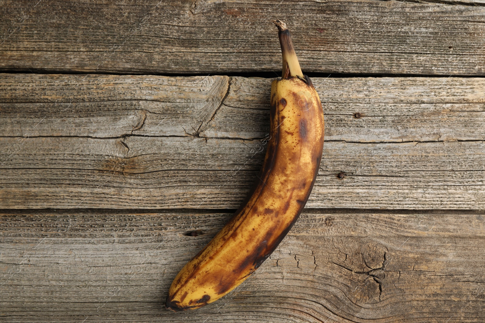 Photo of Overripe banana with dark spots on wooden table, top view