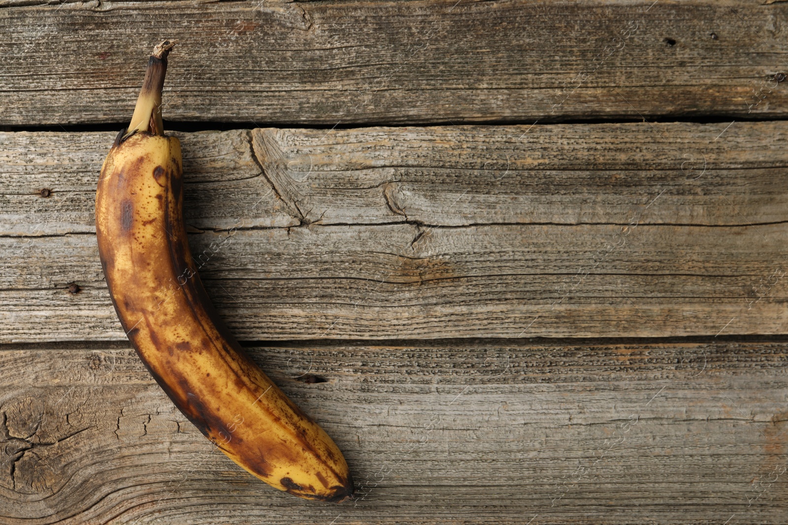 Photo of Overripe banana with dark spots on wooden table, top view. Space for text