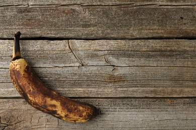 Photo of Overripe banana with dark spots on wooden table, top view. Space for text