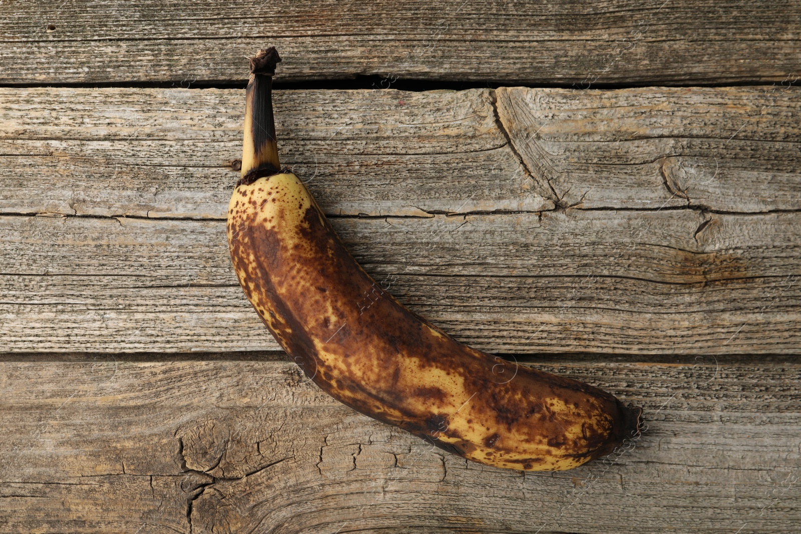 Photo of Overripe banana with dark spots on wooden table, top view