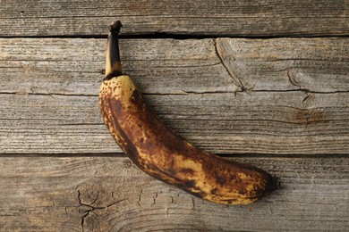 Photo of Overripe banana with dark spots on wooden table, top view