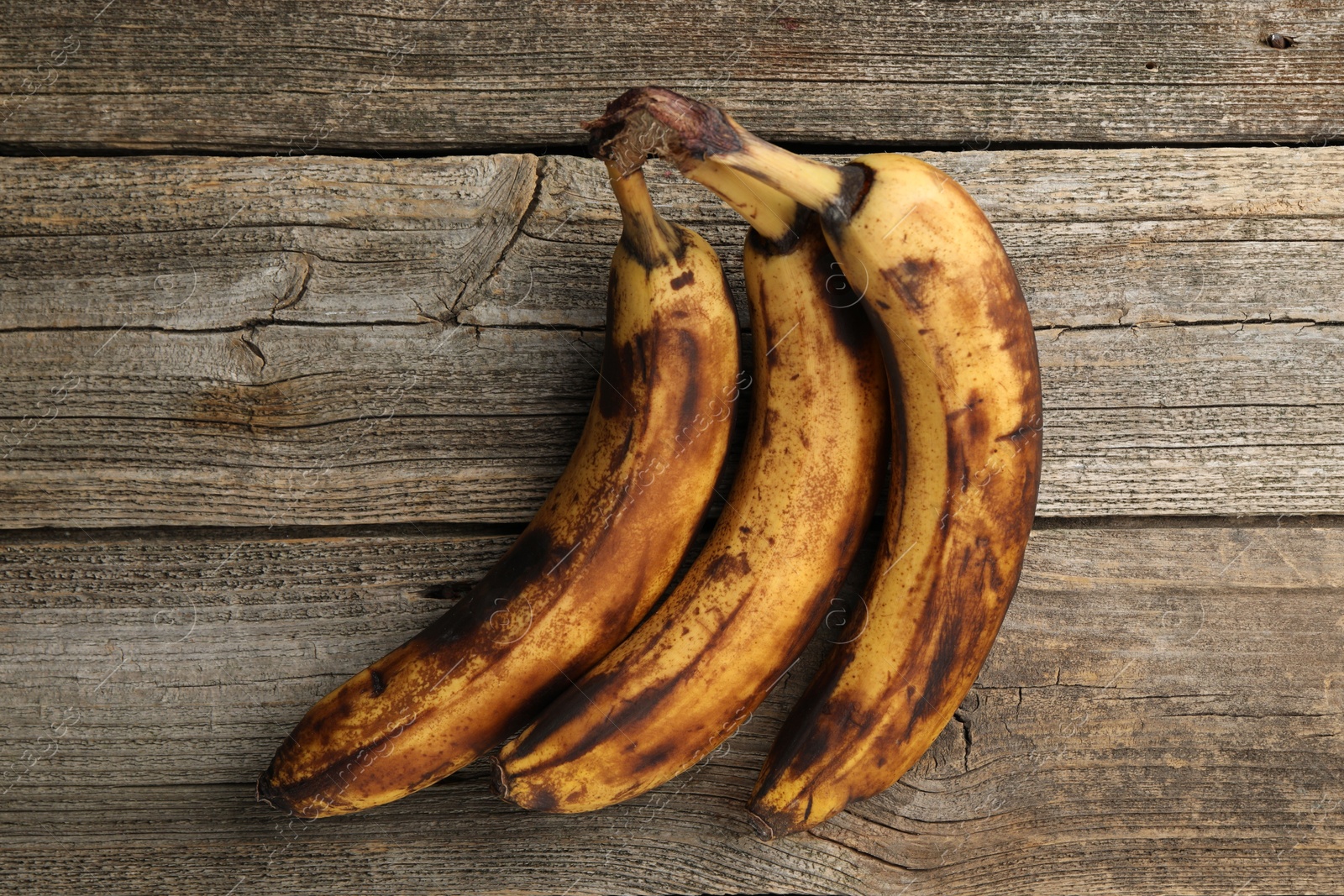 Photo of Bunch of ripe bananas with dark spots on wooden table, top view