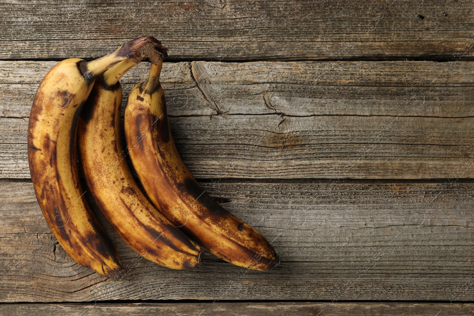 Photo of Bunch of ripe bananas with dark spots on wooden table, top view. Space for text