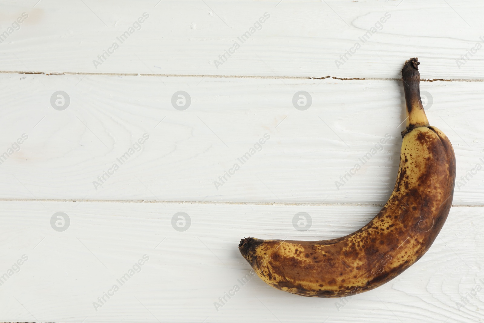 Photo of Overripe banana with dark spots on white wooden table, top view. Space for text