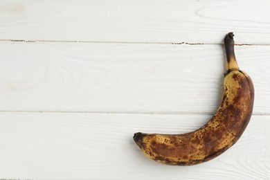 Overripe banana with dark spots on white wooden table, top view. Space for text