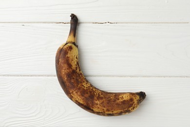 Photo of Overripe banana with dark spots on white wooden table, top view