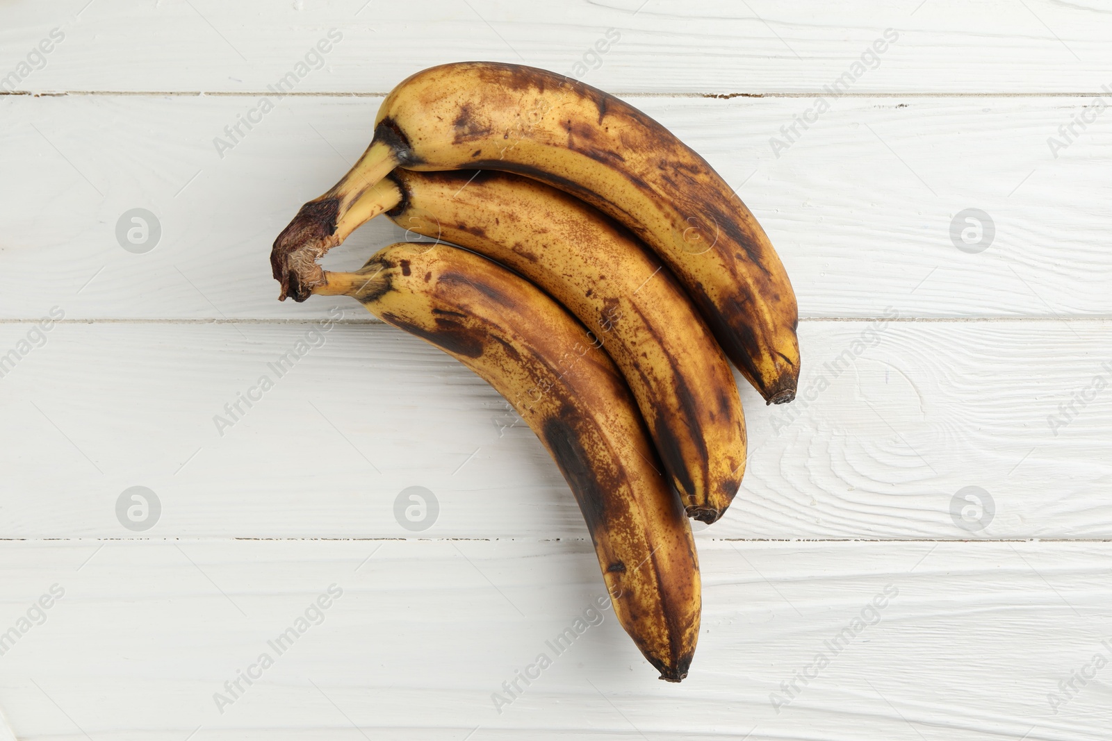 Photo of Bunch of ripe bananas with dark spots on white wooden table, top view