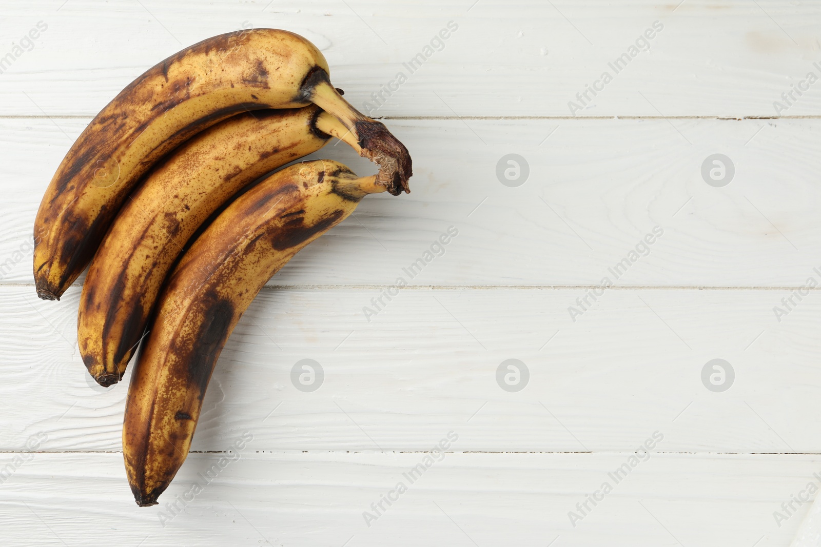 Photo of Bunch of ripe bananas with dark spots on white wooden table, top view. Space for text