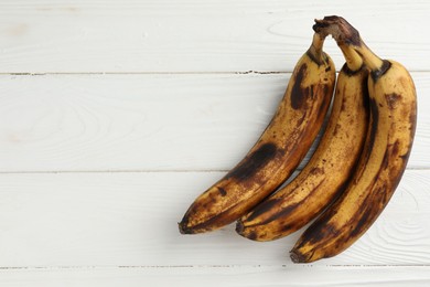 Photo of Bunch of ripe bananas with dark spots on white wooden table, top view. Space for text