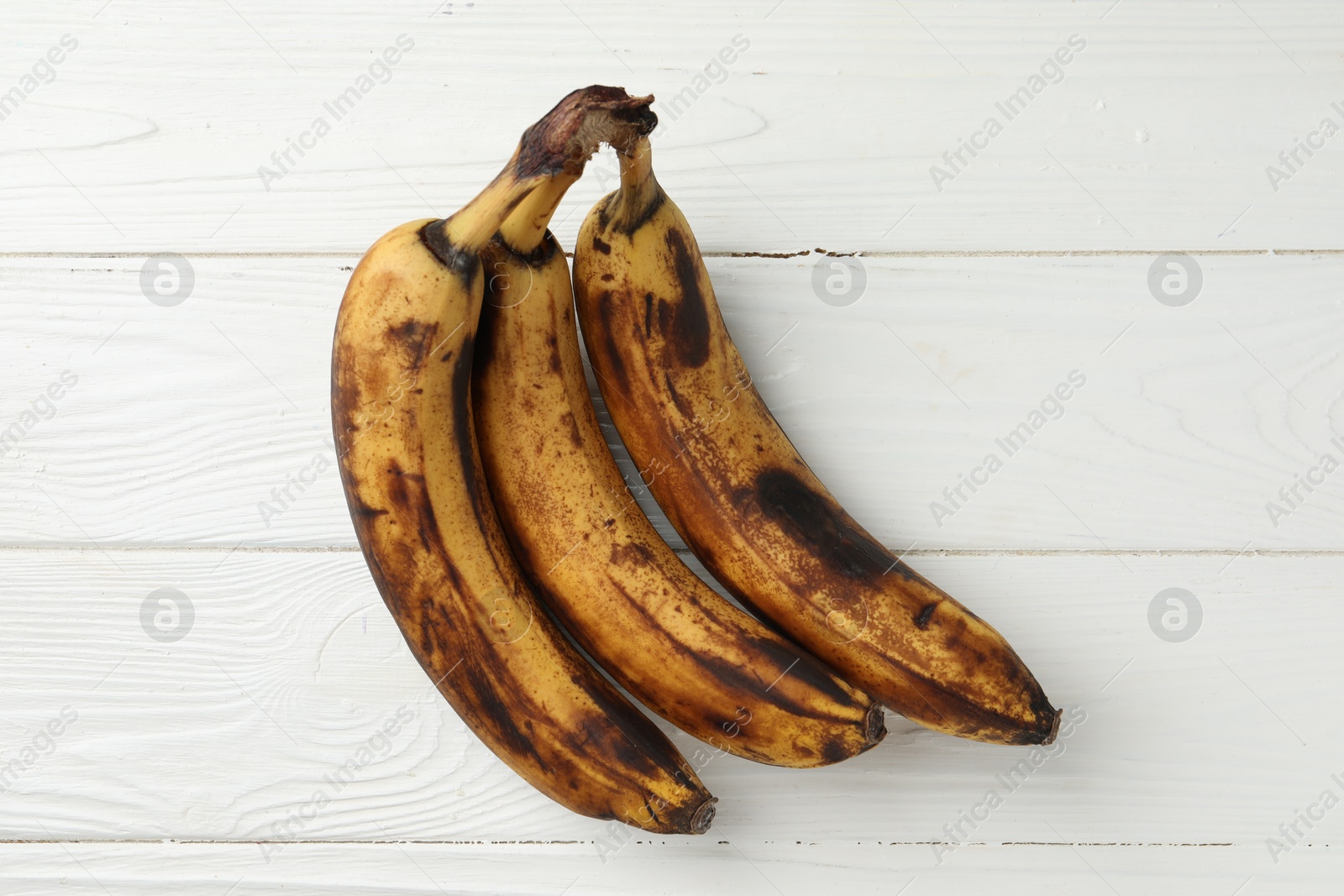 Photo of Bunch of ripe bananas with dark spots on white wooden table, top view