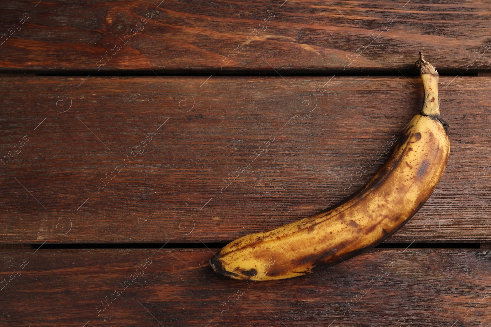 Photo of Overripe banana with dark spots on white wooden table, top view. Space for text