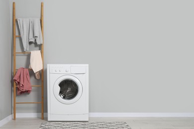 Photo of Washing machine, ladder and laundry near grey wall indoors, space for text