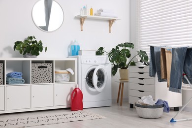 Photo of Washing machine, furniture, detergents, laundry, houseplants and drying rack indoors