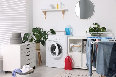 Photo of Washing machine, furniture, detergents, laundry, houseplants and drying rack indoors